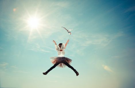 Girl being lifted up by a paper bird into the sky