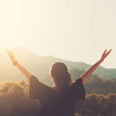 woman with arm raised in joy towards the sun