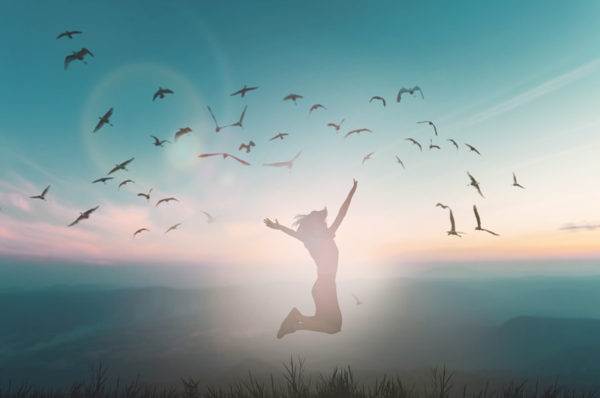 woman jumping in front of a sunrise with birds taking flight showing freedom in letting go