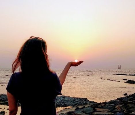 woman on the beach with hand holding the sun to accept ending of day