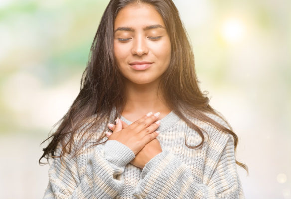 Woman with hands over heart, eyes closed, smiling in kindness towards herself
