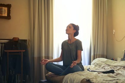 woman sitting cross-legged on her bed with eye closed and breathing