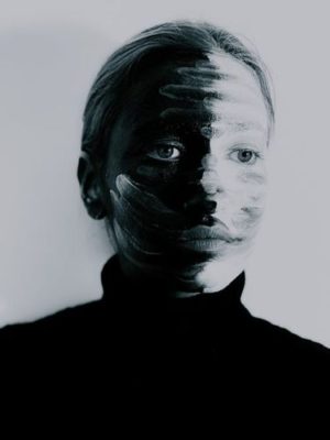 woman with her face painted half black and half white, opposite