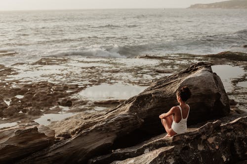 Woman sitting on a rock looking out at ocean with contemplation