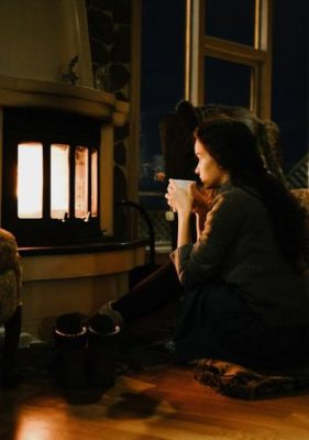 woman sitting quietly by a fire sipping tea