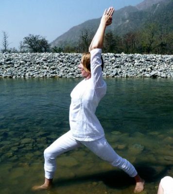 woman in wearing white in warrior one pose in a calm river