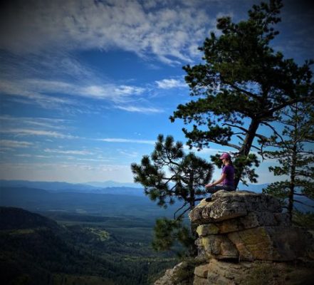 Woman sitting on a rock outcropping over looking a magnificent view meditating