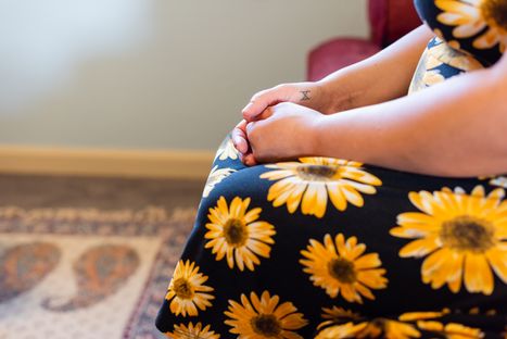 woman in a floral dress, sitting with palms in hands peacefully