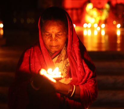 Indian woman looking down at a candle in her hand leaving an altar