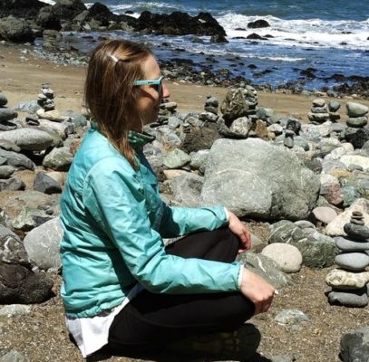 Woman sitting cross-legged on a rocky beach contemplating