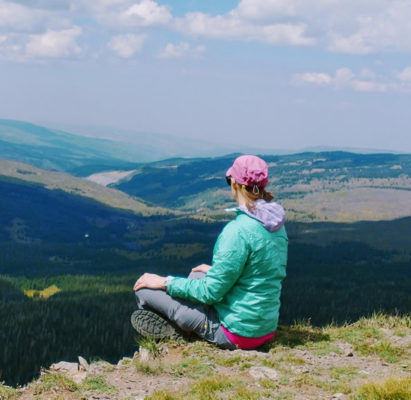 Woman sitting cross-legged overlooking a valley peacefully