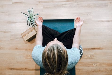 overhead view of woman sitting cross-legged on yoga mat, palms facing up on knees in meditation