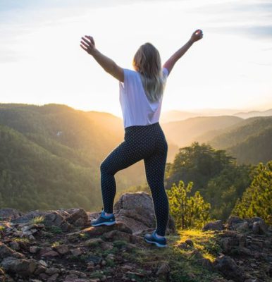 woman at the top of a mountain, arms out stretched feeling accomplished from the effort