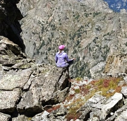 woman sitting in meditation on a rock surrounded by mountains