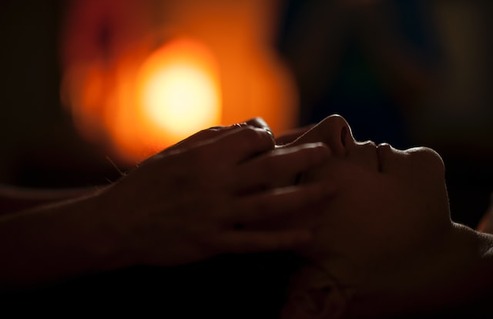 person receiving face massage with a calming, glowing candle light in background