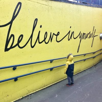 Young child looking up at a mural that states, "believe in yourself."