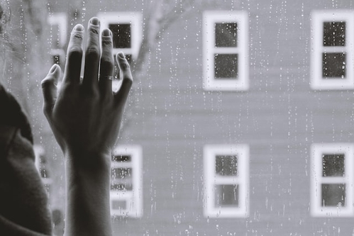 black and white photo of person's hand on a rain streaked window looking out