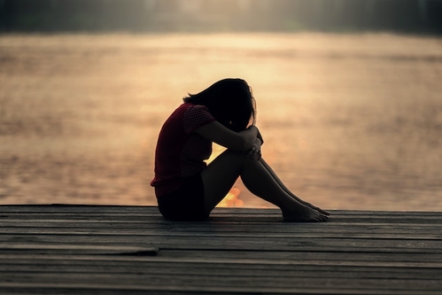 Woman sitting on a dock with arms resting on knees, head bowed in feelings of sadness