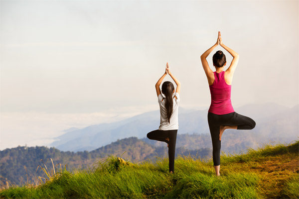 mother and daughter in tree pose in a grassy meadow looking over a valley