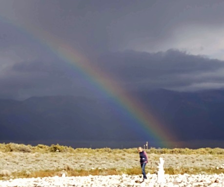 person walking a labyrinth sun shining with dark clouds around mountains and rainbow