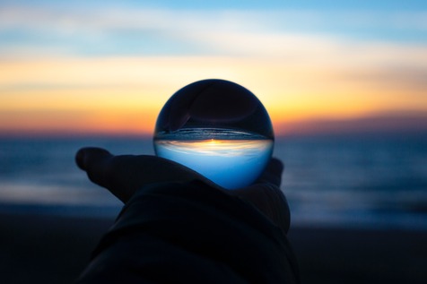 hand holding a glass sphere that sharpens the blurred background sunset showing clarity