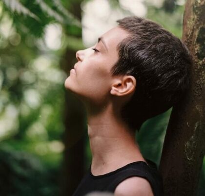 headshot of woman leaning against a tree, eyes closed, breathing