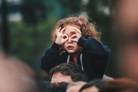 young girl on her father's shoulders looking through hand binoculars with cuirosity