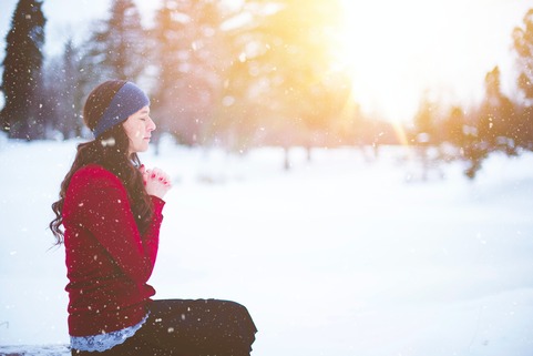 woman sitting in meditation, hands together at heart as it's snowing and the sun is setting