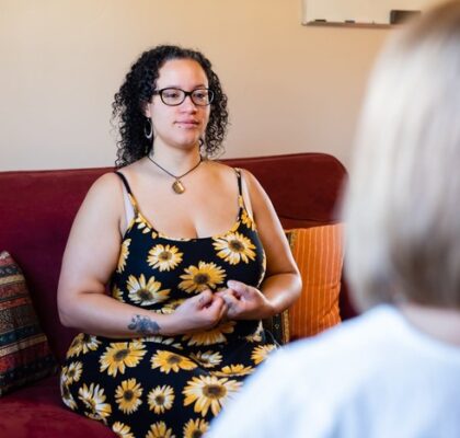 woman seated with hands in a mudra led by her yoga-base counselor