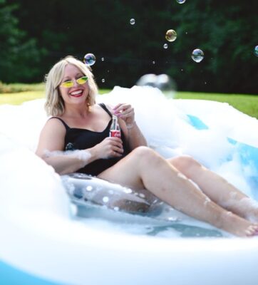 white woman in a blow up outdoor pool with bubbles and smiling