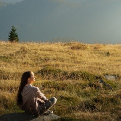 white woman sitting on a rock in a mountain meadow at peace