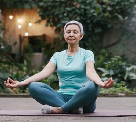 older woman sitting cross-legged in meditation on yoga mat