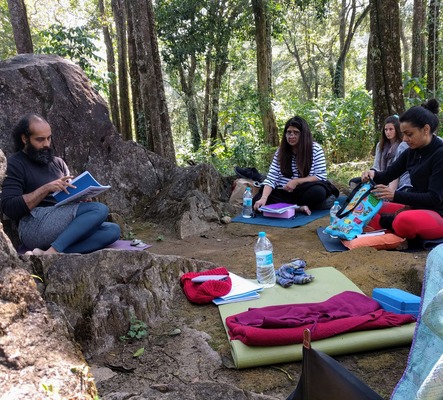 This author's Yoga teacher giving a lesson with students gathered around him in the forest in Southern India