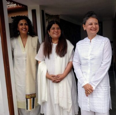 Three women Yoga students dressed in white for a ceremony smiling and looking right