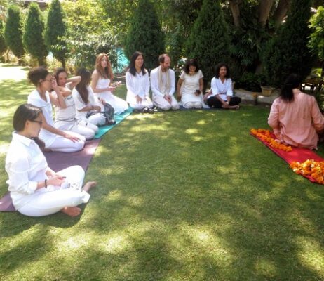 group of yoga students in white witting with their teacher in orange