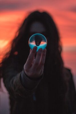 woman blurred with sunset background while holding a glass sphere that reflects her with clarity