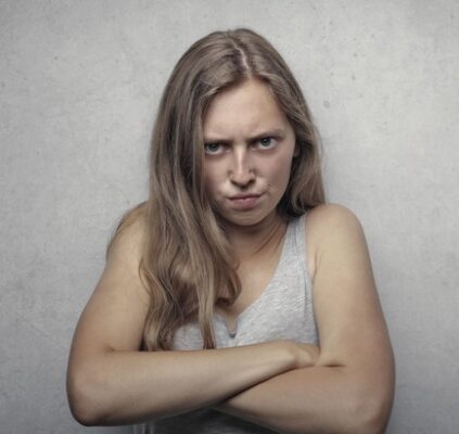 woman with long hair and grey tank top with arms folded and an angry scowl