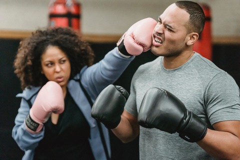 woman in pink boxing gloves punching a man in boxing gloves on the left side of his face