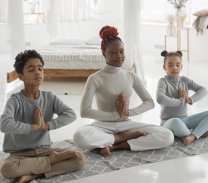 mother and her two children sitting next to each other, cross-legged in meditation with hands at heart