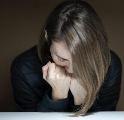 woman sitting bent over with head resting on her fists feeling sad and upset