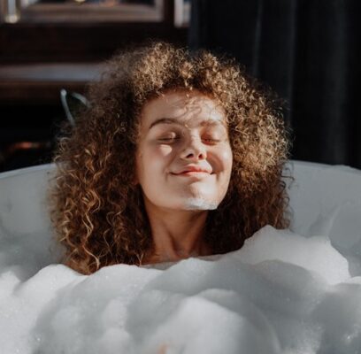 woman in a bubble bath with eyes closed and smiling with contentment