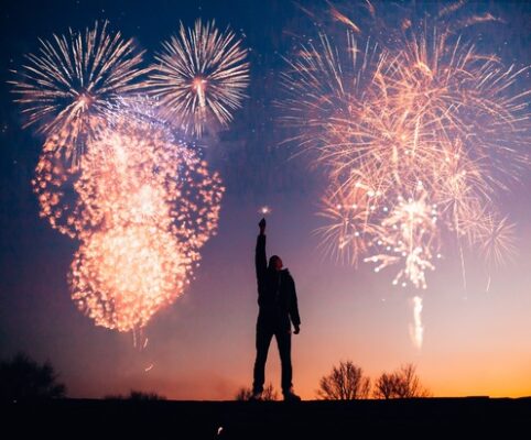 Fourth of July fireworks with person looking up, arm raised in strength, holding a sparkler