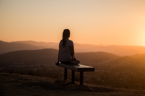 woman sitting on a bench overlooking a hilly valley at sunset with inner contemplation