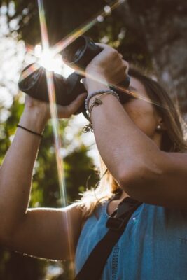 woman looking through binoculars searching with sunlight shining behind her 