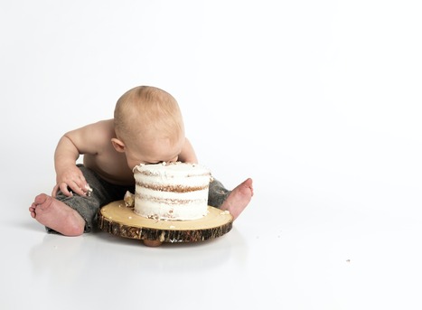 baby sitting and bending forward with its face in a cake overindulging