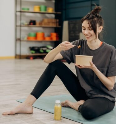 woman smiling and sitting on the floor slowly eating with chop sticks and enjoying her meal 