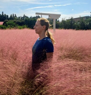 Author standing in field of pink grass, eyes closed and listening 