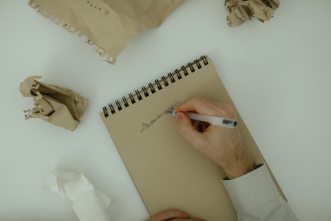 person crossing out what they wrote with crumpled attempts surrounding the notepad unsure what to write