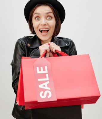 woman with a look of excitement holding two read shopping boxes and a sale tag