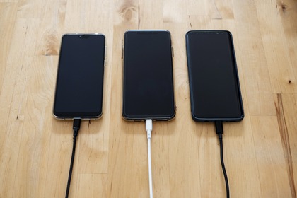 three cell phones on a wooden table being charged